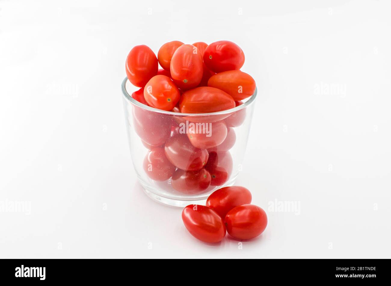 Pomodori ciliegini (mini) nella tazza di vetro. Ciliegia o mini pomodori in vetro isolato su sfondo bianco Foto Stock