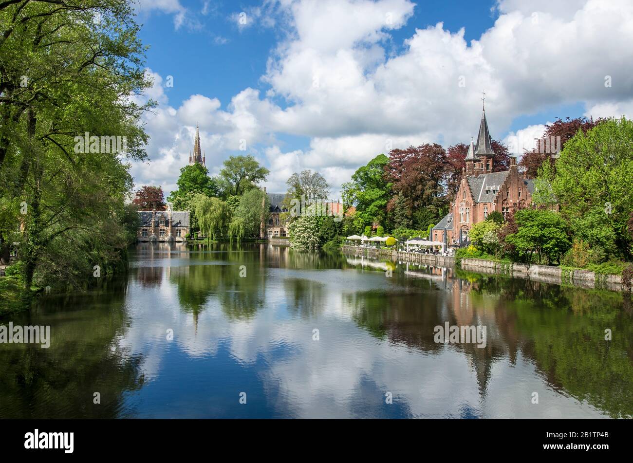 Vista sul tranquillo spazio verde pubblico con il lago Minnewater e il piccolo castello di Bruges durante la giornata di sole in primavera, in Belgio Foto Stock