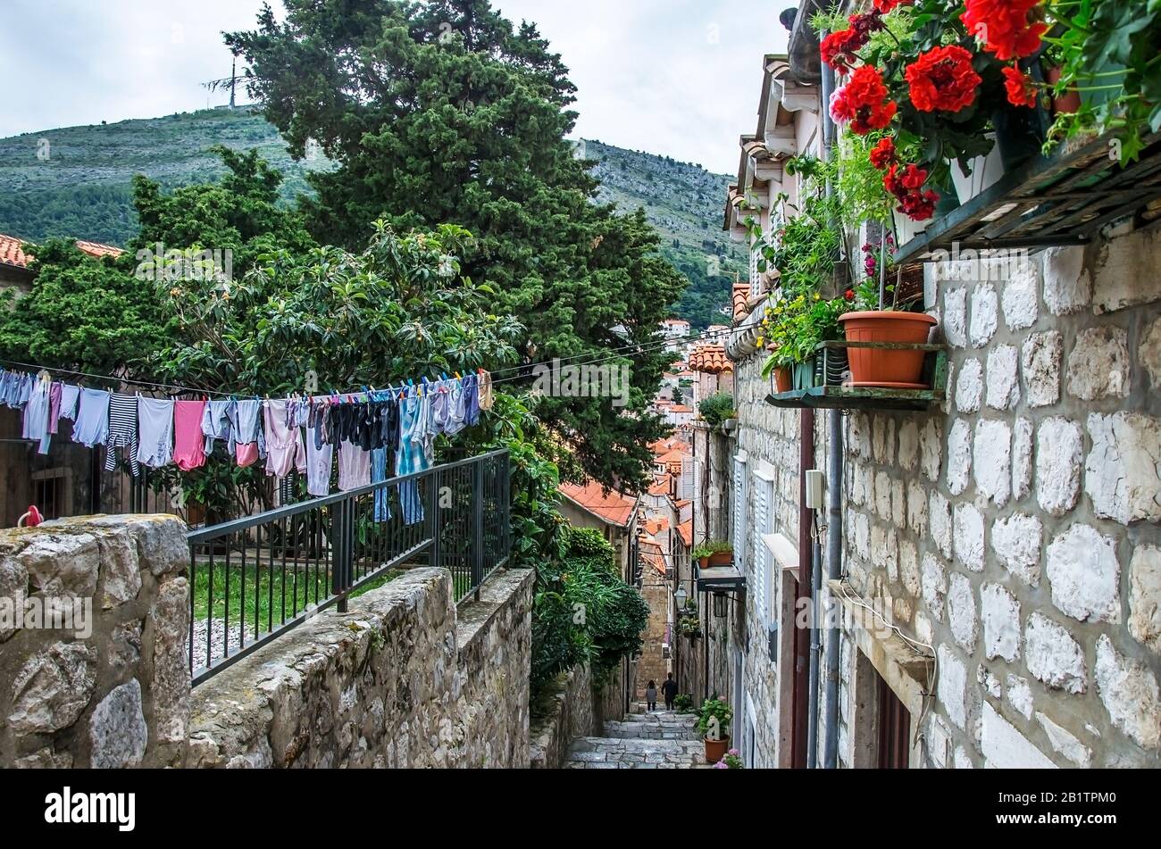 Vista sulla strada stretta con edifici in pietra, fiori, appendiabiti e scale lavanderia nella città vecchia di Dubrovnik. Lavanderia a strapiombo su un tipico croato Foto Stock