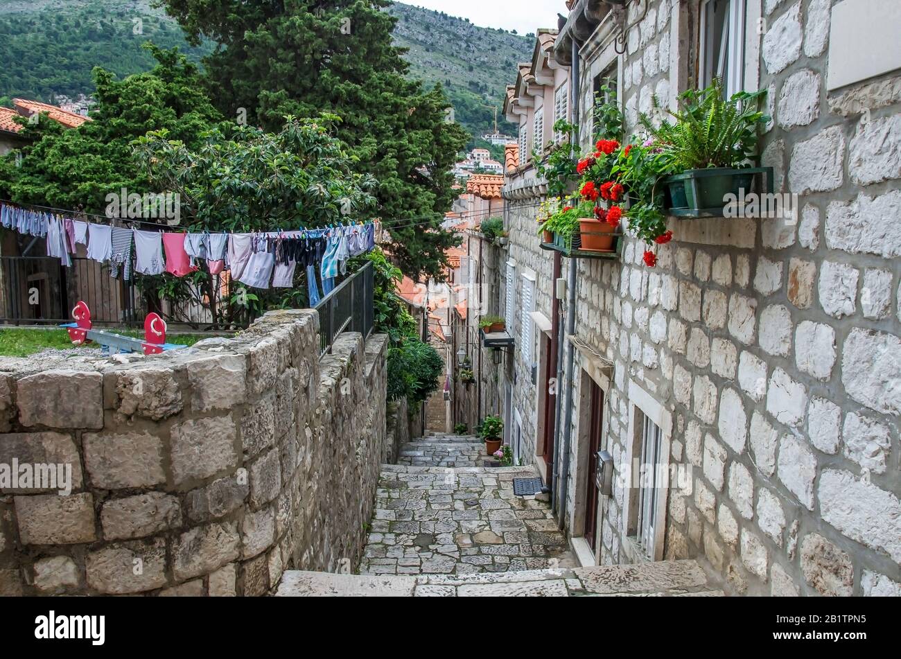 Vista sulla strada stretta con edifici in pietra, fiori, appendiabiti e scale lavanderia nella città vecchia di Dubrovnik. Lavanderia a strapiombo su un tipico croato Foto Stock
