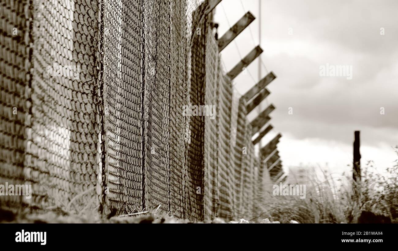 Concentratevi su una piccola area della recinzione per cercare di ottenere un'atmosfera drammatica e cinematografica per la foto, con le nuvole pesanti e la recinzione metallica Foto Stock