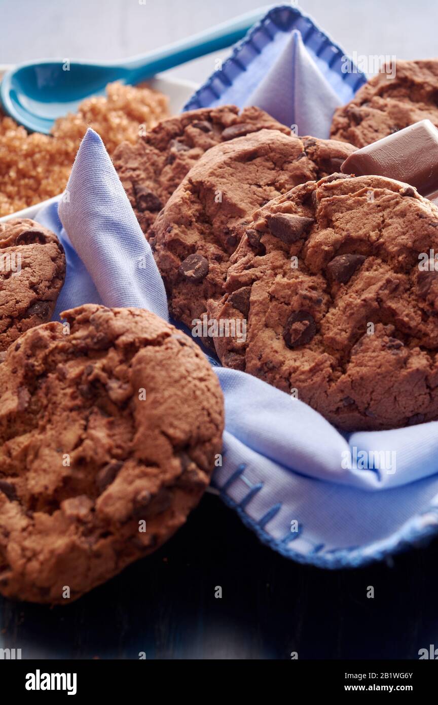 piatto di biscotti di cacao, zucchero di canna marrone e cioccolato, con tonalità blu su tovagliolo, tavolo in legno, tovaglia e cucchiaio Foto Stock