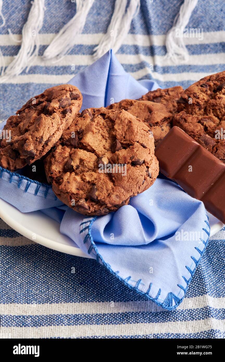 piatto di biscotti di cacao, zucchero di canna marrone e cioccolato, con tonalità blu su tovagliolo, tavolo in legno, tovaglia e cucchiaio Foto Stock