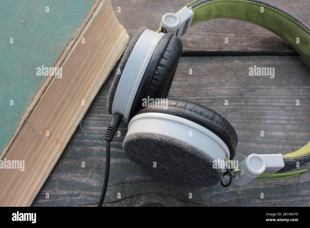 Vecchio libro shabby e cuffie su un tavolo di legno ruvido, all'aperto. Vista dall'alto Foto Stock