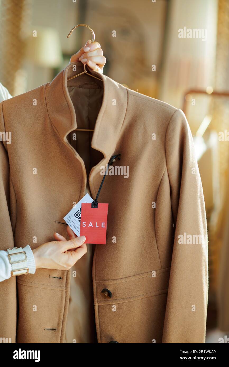 Primo piano su femmina in negozio di moda moderna esamina il prezzo di vendita tag sul cappotto. Foto Stock