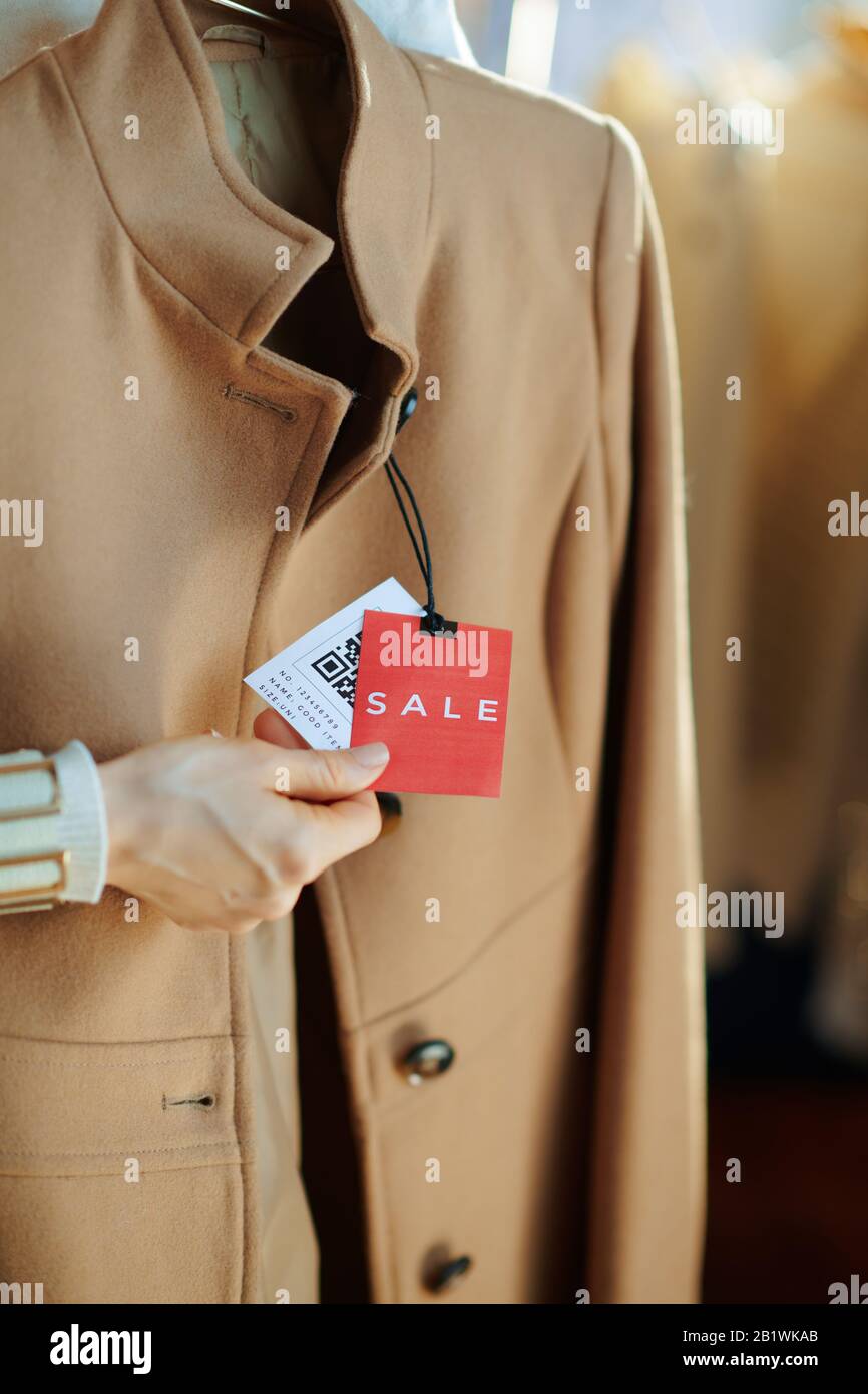 Closeup su donna in negozio di moda moderna esamina il prezzo di vendita tag su cappotto beige. Foto Stock