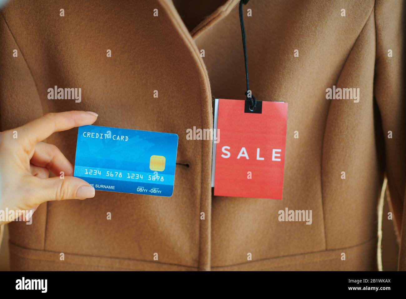 Primo piano su cappotto beige con prezzo di vendita rosso tag e carta di credito blu in moderno showroom moda. Foto Stock