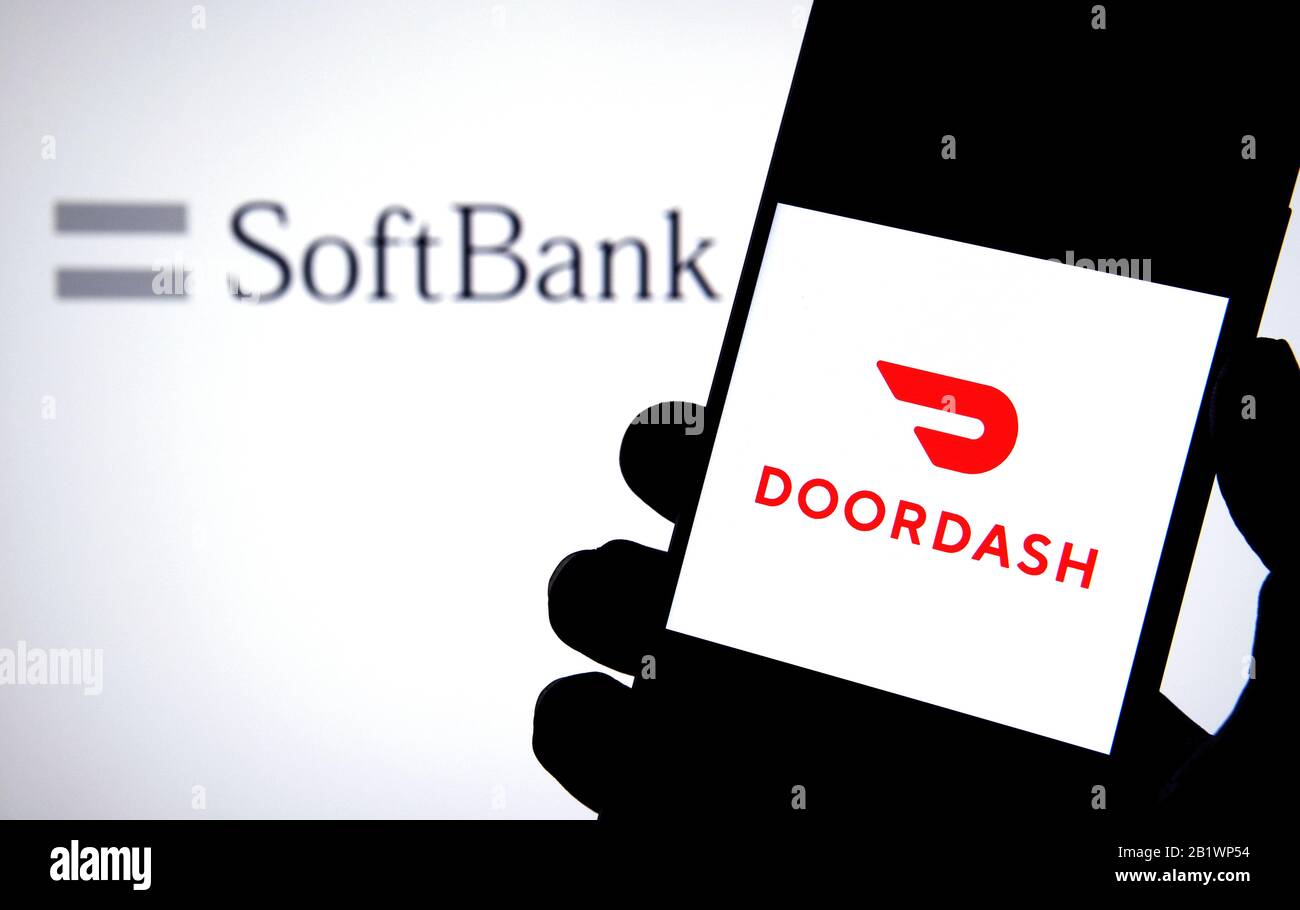 Logo Doordash aziendale su uno smartphone tenere a portata di mano con il logo SoftBank sullo schermo del notebook sfocato dietro. Concetto. Non un montaggio, foto reale. Foto Stock