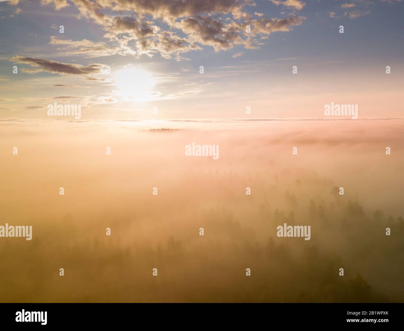 Foto drone sopra nuvole molto spesse nubi nebbiose alba sul paesaggio forestale e villaggio nel Nord Svezia - luce solare dorata Foto Stock