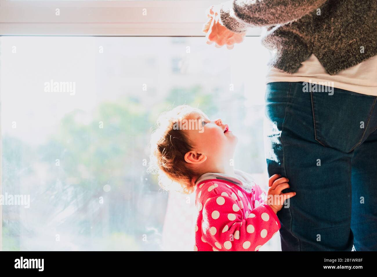 Il bambino guarda la madre abbracciando le gambe, la scena familiare domestica. Foto Stock