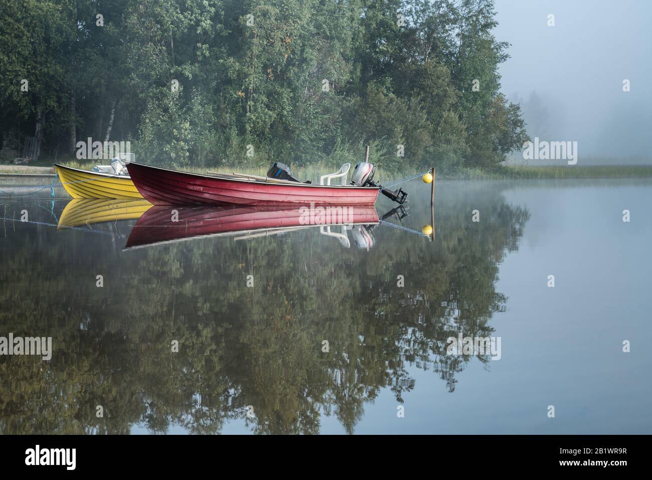 Due barche ormeggiate al lago foggy, alba precoce, alberi, riflesso cielo in acqua calma, bella scena rilassante, paesaggio europeo, natura settentrionale Foto Stock