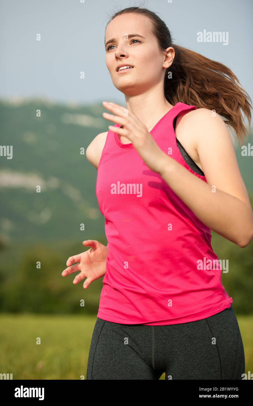 Bella giovane donna allenamento all'aperto corre attraverso prato all'inizio dell'estate Foto Stock