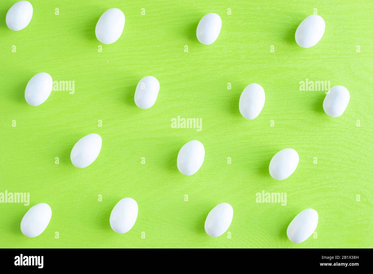 Dolci bianchi glassati piatto pattern rhythm piccole caramelle con mandorla su sfondo verde chiaro. Foto Stock
