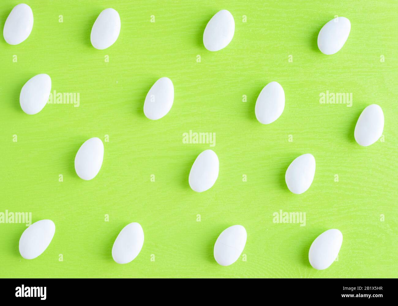 Caramelle di mandorle bianche ovali glassate per bonbonnieres ripetizione motivo luminoso foto su sfondo verde chiaro. Vista dall'alto Foto Stock