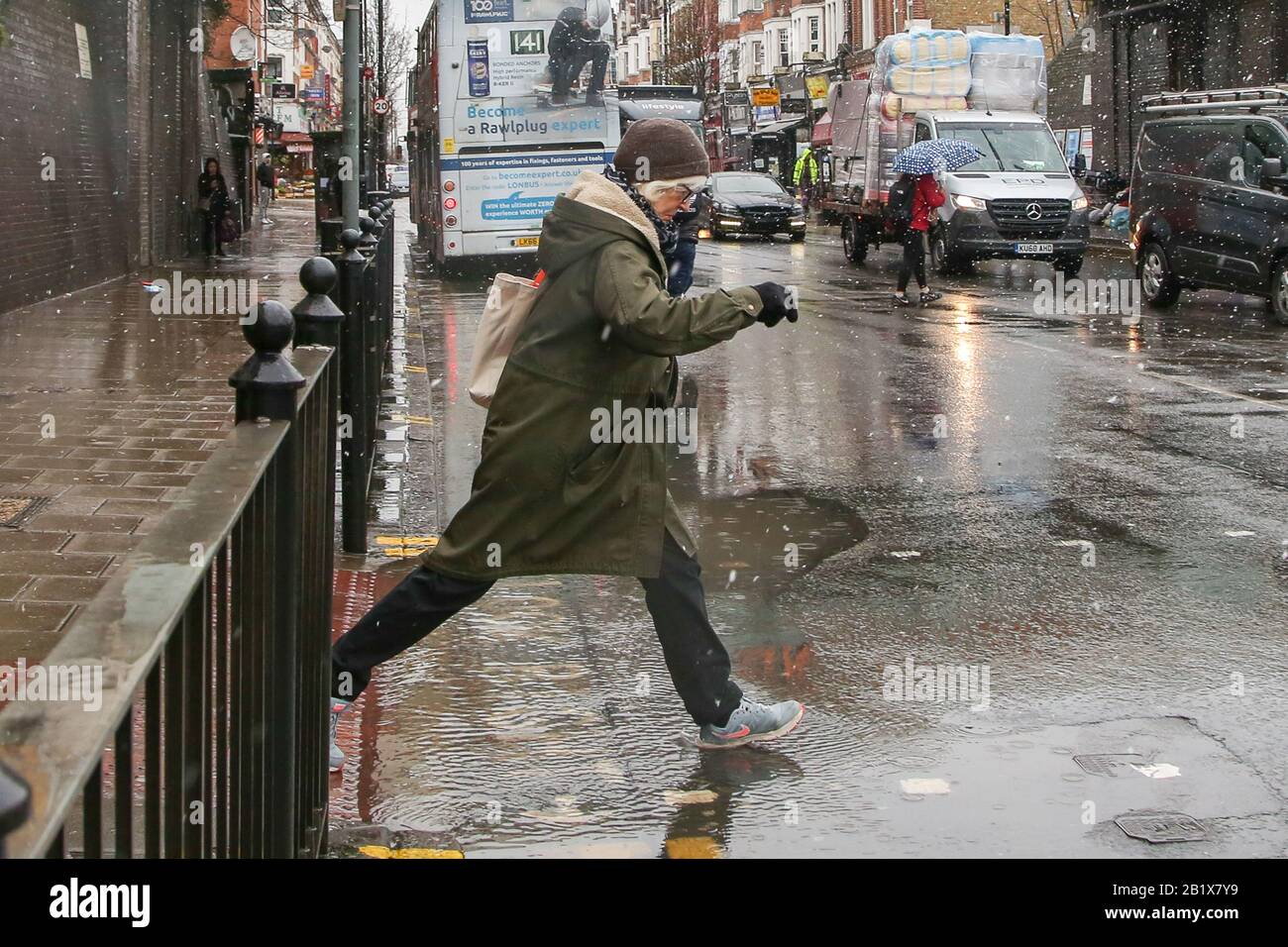 Londra, Regno Unito. 27th Feb, 2020. Una donna salta sopra una pozza d'acqua durante una nevicata nel nord di Londra. Credit: Sopa Images Limited/Alamy Live News Foto Stock