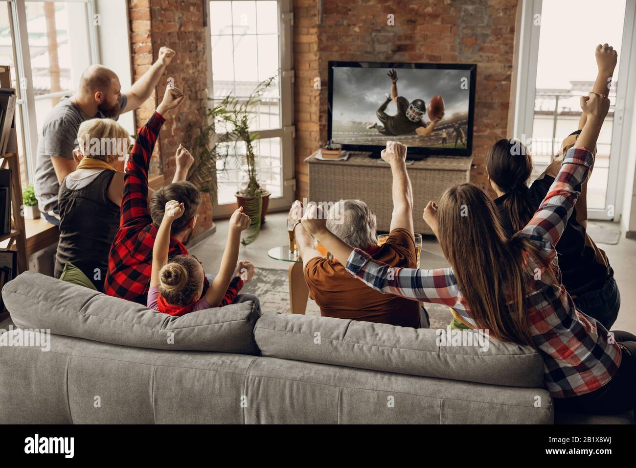 Vittoria. Una famiglia entusiasta e felice guarda la partita di football  americano, campionato sul divano a casa. Fan emozionali che acclamano per  la squadra nazionale preferita. Figlia, papà e nonno. Sport, TV,