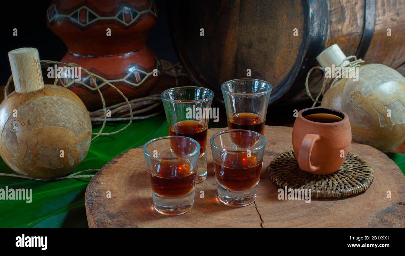 Quattro piccole tazze di vetro con liquore fatto a mano su un tronco di legno con fondo a botte e artigianato dell'Amazzonia ecuadoriana su tavolo di legno Foto Stock