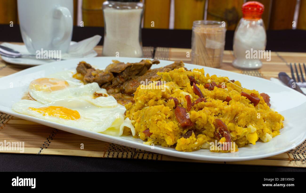 TIGRILLEO è un piatto tipico composto da banana verde macinato con formaggio servito in un piatto verde su un tavolo viola accompagnato da uova fritte e carne Foto Stock