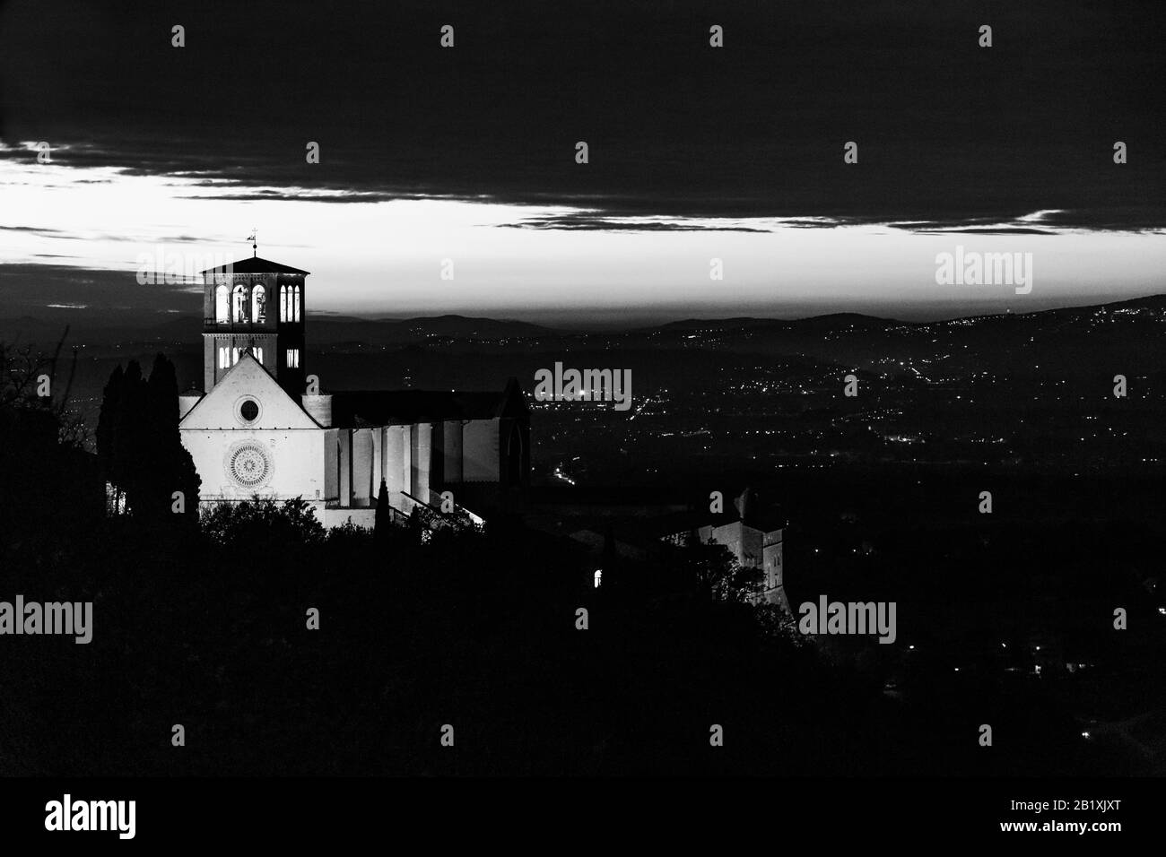 Vista della chiesa papale di San Francesco ad Assisi di notte, con le luci della città sullo sfondo Foto Stock