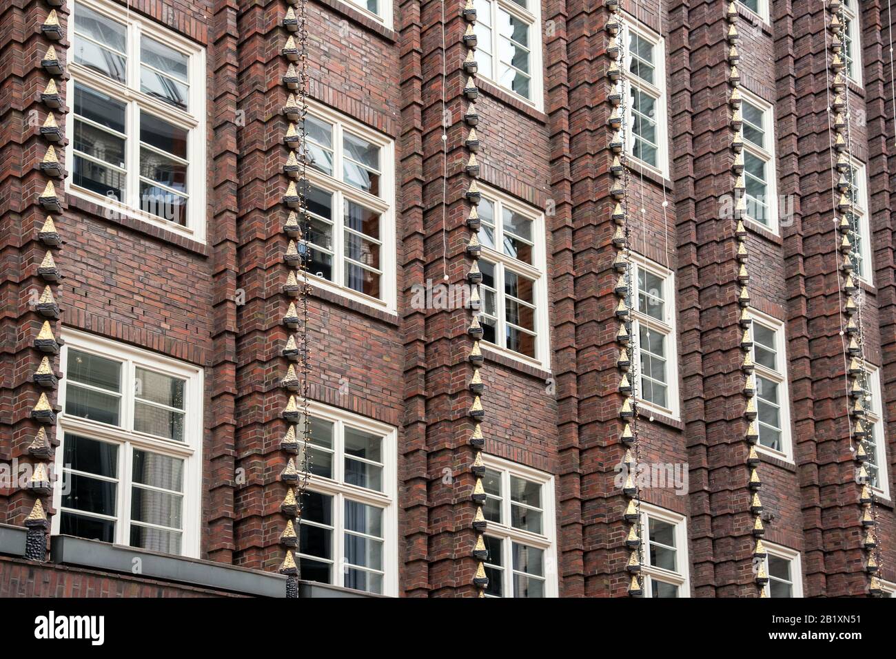 Facciata in mattoni marroni dell'edificio del palazzo con finestre e finestre verticali decorative, vista da basso angolo in pieno telaio Foto Stock