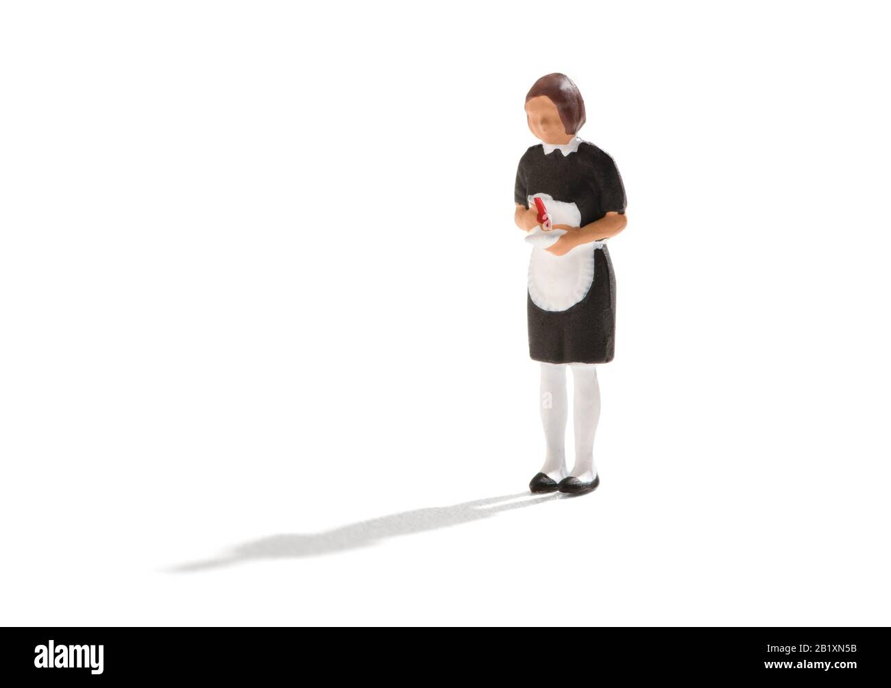 Figura in miniatura di una cameriera o di un aiuto assunto in una uniforme nera con grembiule bianco su uno sfondo bianco con spazio copia Foto Stock