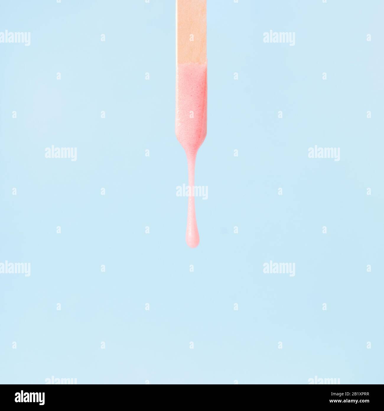cera rosa liquida o pasta di zucchero per la depilazione scarichi dal bastone su sfondo blu. Il concetto di depilazione, ceratura, pelle liscia zuccherata, bellezza Foto Stock