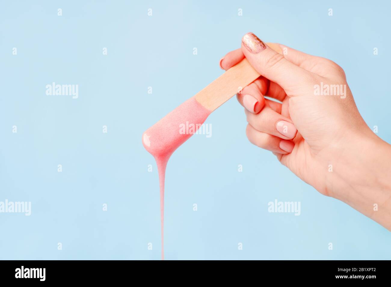 cera rosa perla liquida o pasta di zucchero per depilazione scarichi dal bastone su sfondo blu. Il concetto di depilazione, ceratura, pelle liscia zuccherata Foto Stock