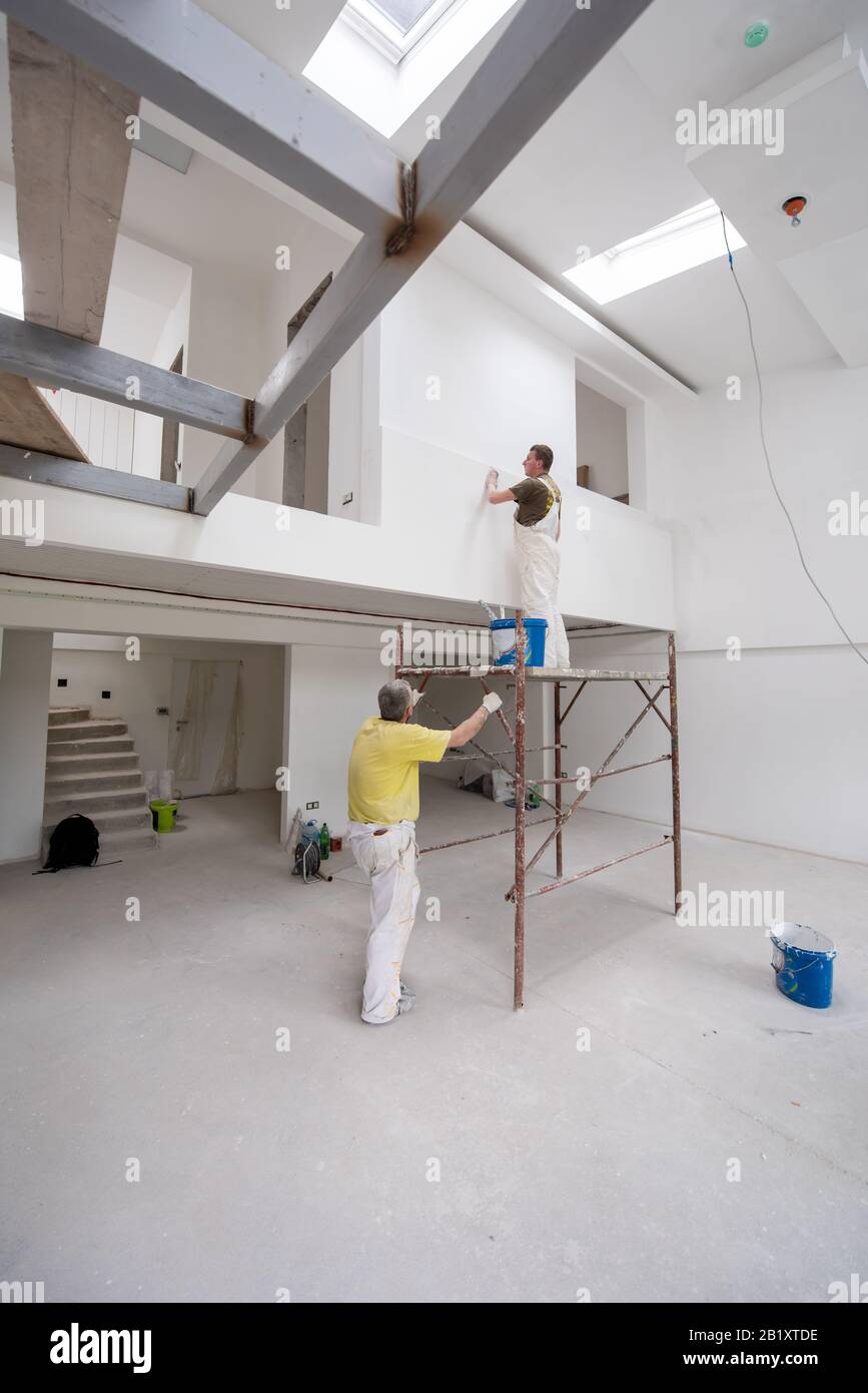 giovane operaio edile professionale che utilizza impalcature mentre intonacando su pareti in gesso all'interno del nuovo grande appartamento moderno a due livelli Foto Stock