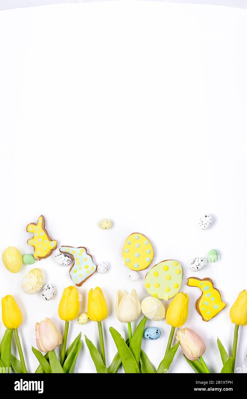 Biscotti di pan di zenzero fatti in casa di Pasqua con glassa, uova decorate e tulipani su uno sfondo bianco / concetto felice di pasqua. Spazio di copia, disposizione piatta, modello Foto Stock