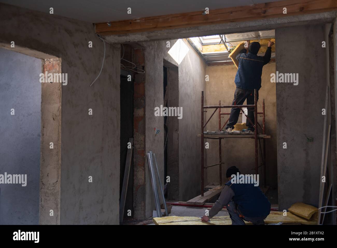 Vista posteriore di operai edili professionisti che installano lo strato di isolamento termico con pannelli di lana minerale sotto il tetto Foto Stock
