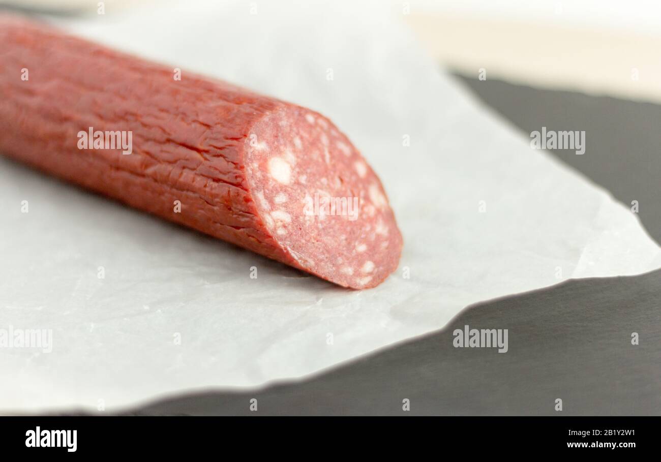 Salame tradizionale. Un pezzo di salsiccia insaccata in carta su una tavola di pietra. Foto Stock