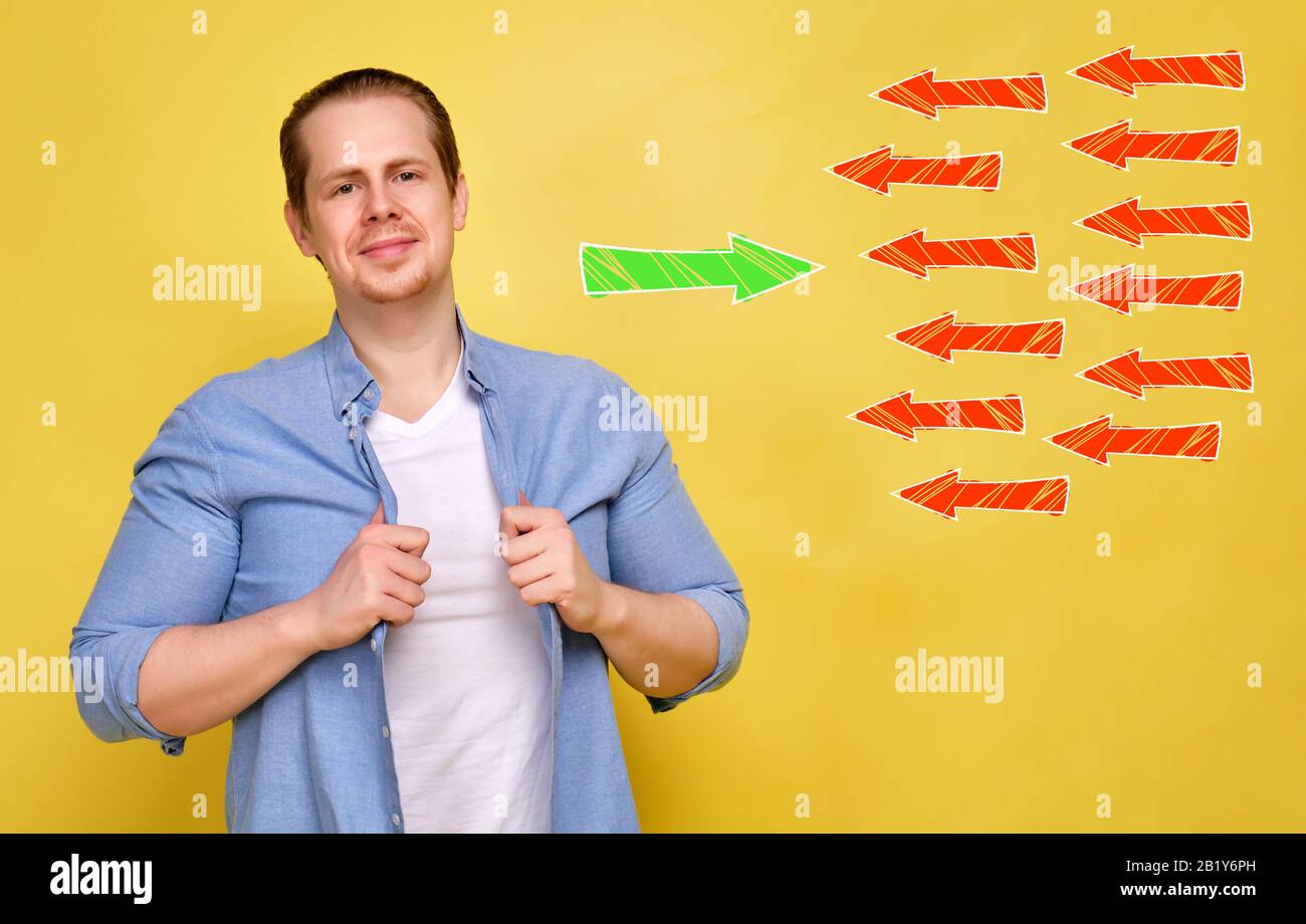 Un uomo in una camicia su sfondo giallo. Il concetto di una persona fiduciosa contro l'opinione pubblica. Freccia verde astratta contro molti rossi. Primo piano Foto Stock