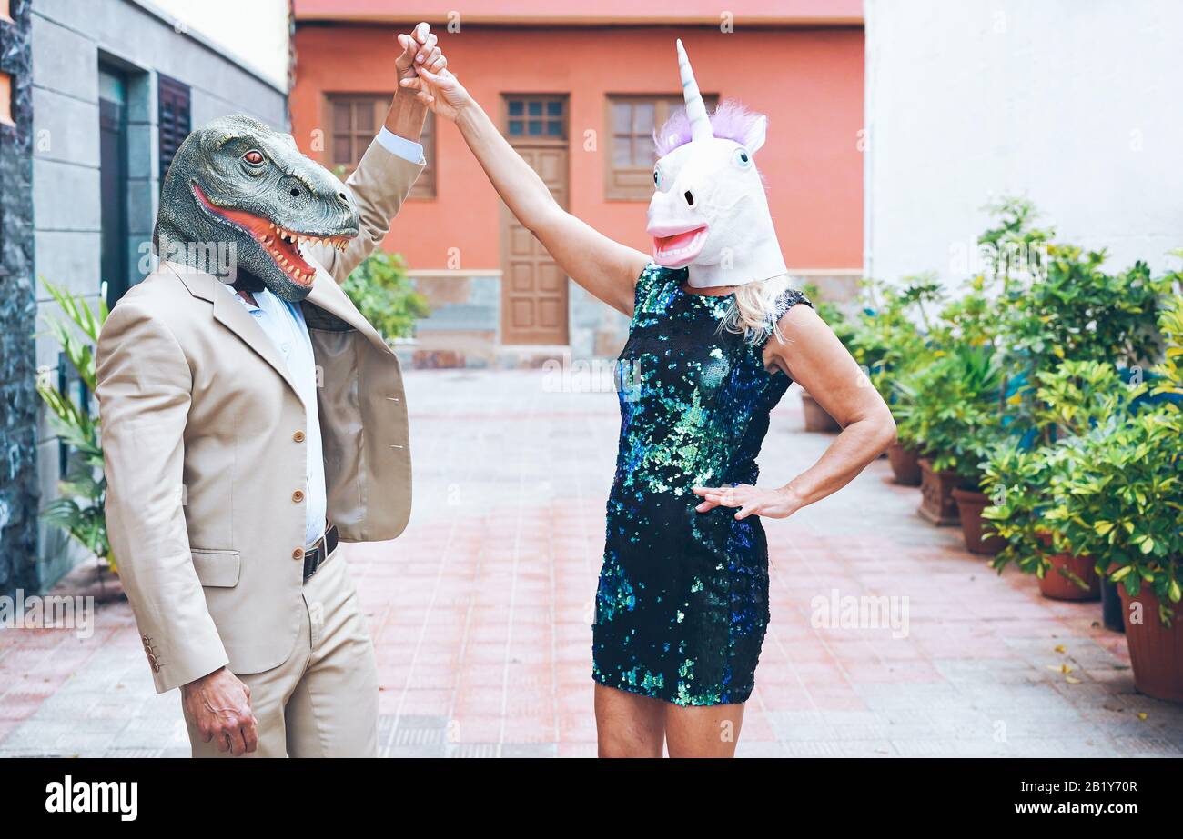 Crazy coppia senior che ballano intorno alla strada della città indossando t-rex e maschera di pollo - Old trendy persone divertirsi insieme - Assurdo e divertente tendenza concetto Foto Stock