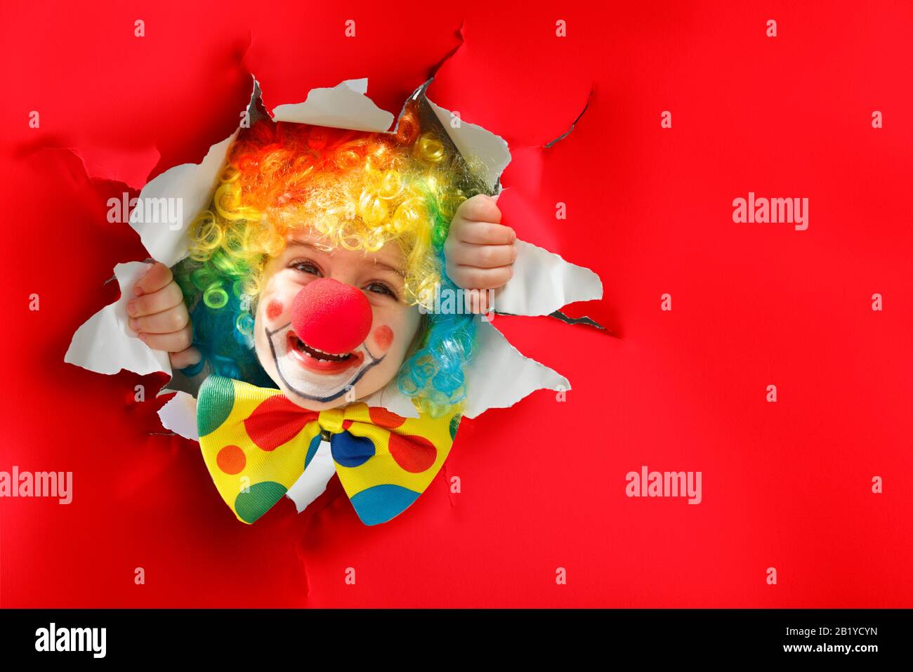 Bambino con il costume di clown che passa attraverso un buco di carta Foto Stock