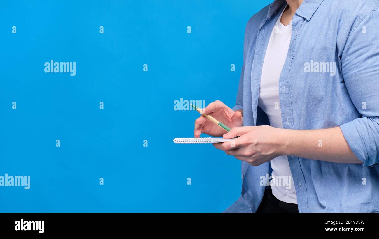 Un uomo in abiti casual su uno sfondo blu senza un volto nella cornice contiene una penna e un notebook. Primo piano. Foto Stock