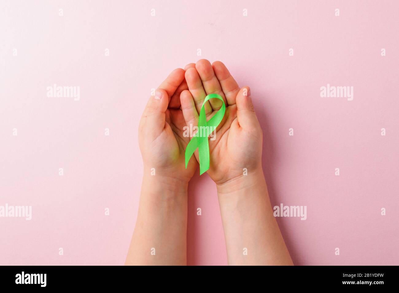 Nastro in raso verde che tiene in mano ai bambini su sfondo rosa. Fegato, consapevolezza del cancro ai reni, Consapevolezza del glaucoma Foto Stock