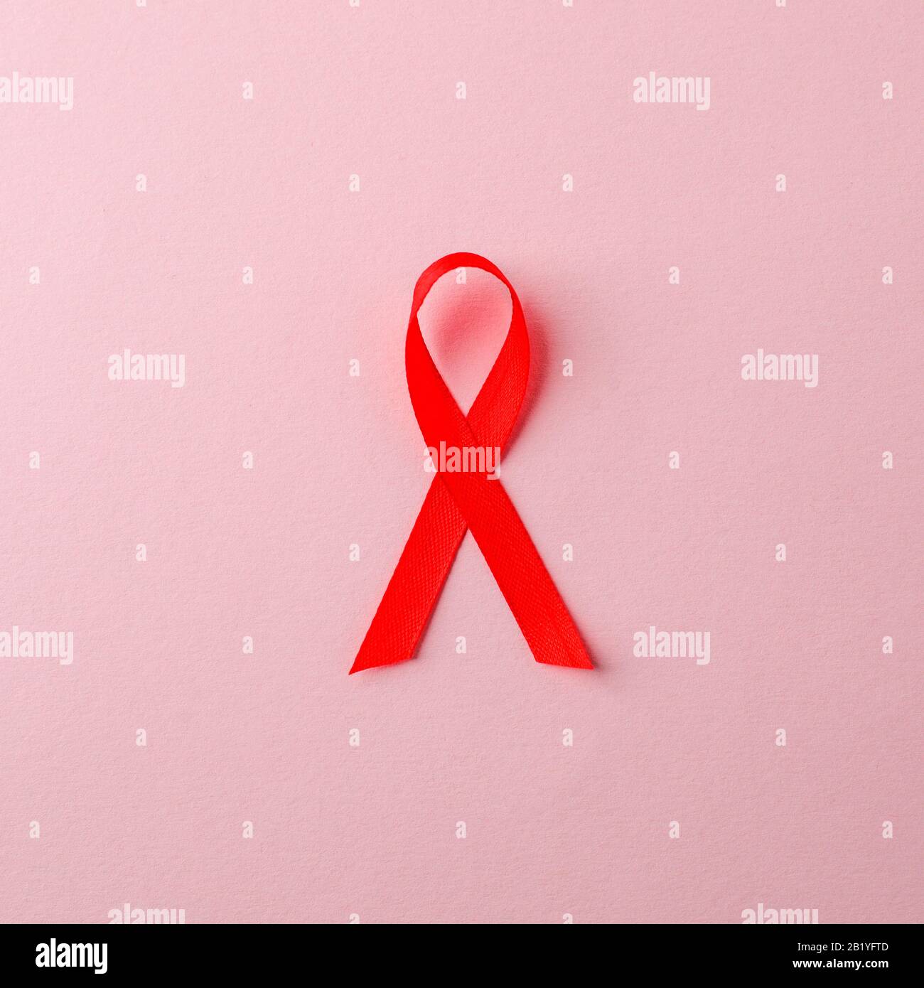 AIDS awareness nastro rosso su sfondo rosa. World AIDS Day Concept, simbolo della malattia del virus dell'immunodeficienza umana Foto Stock
