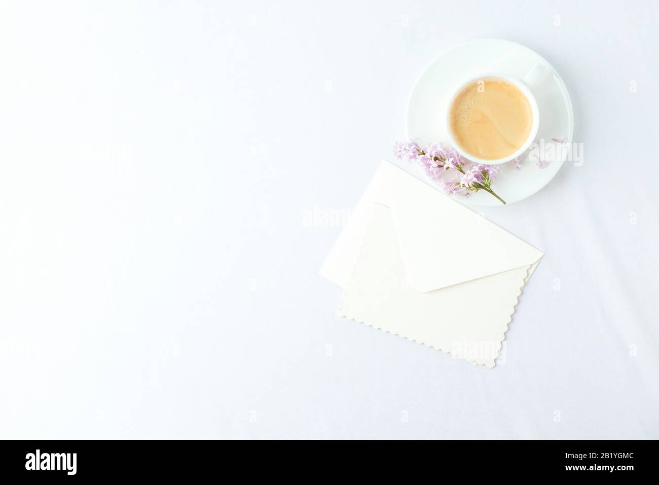 Composizione elegante e minimale con tazzina da caffè e rami lilla, busta su sfondo bianco, colazione femminile al mattino, donna madre giorno, saint valente Foto Stock