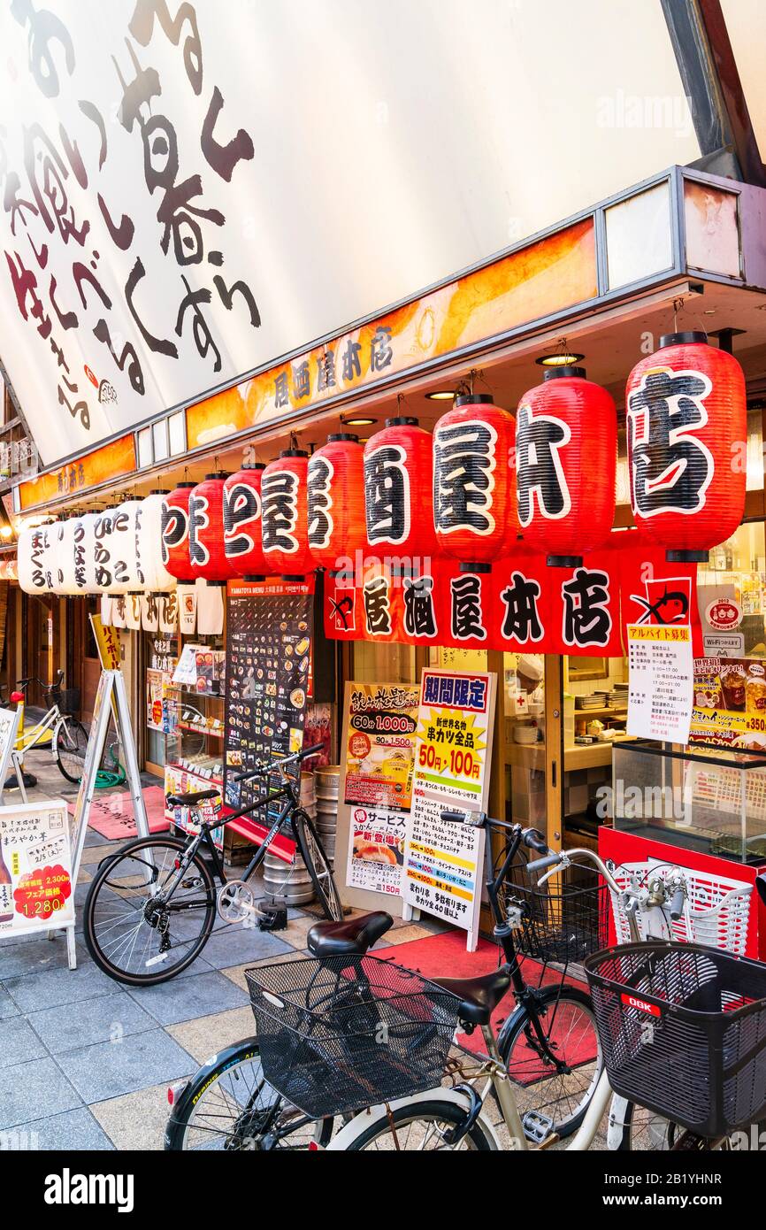 Il ristorante Yamatoya Honten izakaya serve Kushikatsu e sushi. Ingresso al ristorante con biciclette parcheggiate all'esterno, tavole da menu e chochin, lanterne. Foto Stock