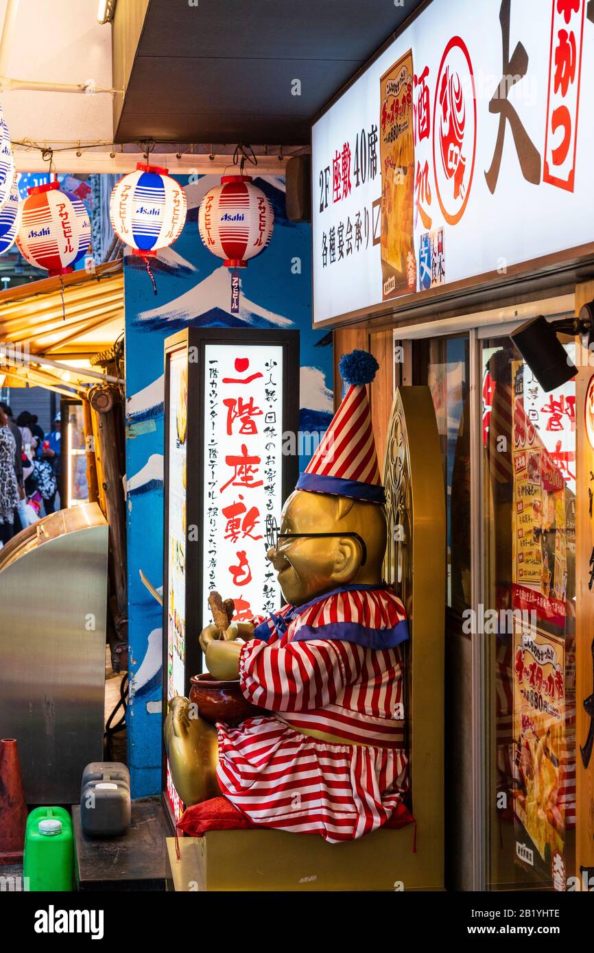 Statua di Billiken fuori dal ristorante Kushikatsu Daikichi a Shinsekai, Osaka. Vista laterale della statua vestita con costume clown e cibo kushikatsu. Foto Stock