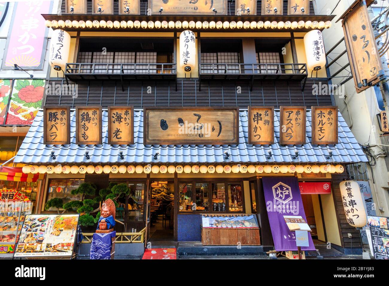 Shinsekai kushikatsu Robatayaki Iruri ristorante facciata esterna. Davanti alla sala da pranzo con ingresso, statua di Billiken e albero giapponese in serata. Foto Stock