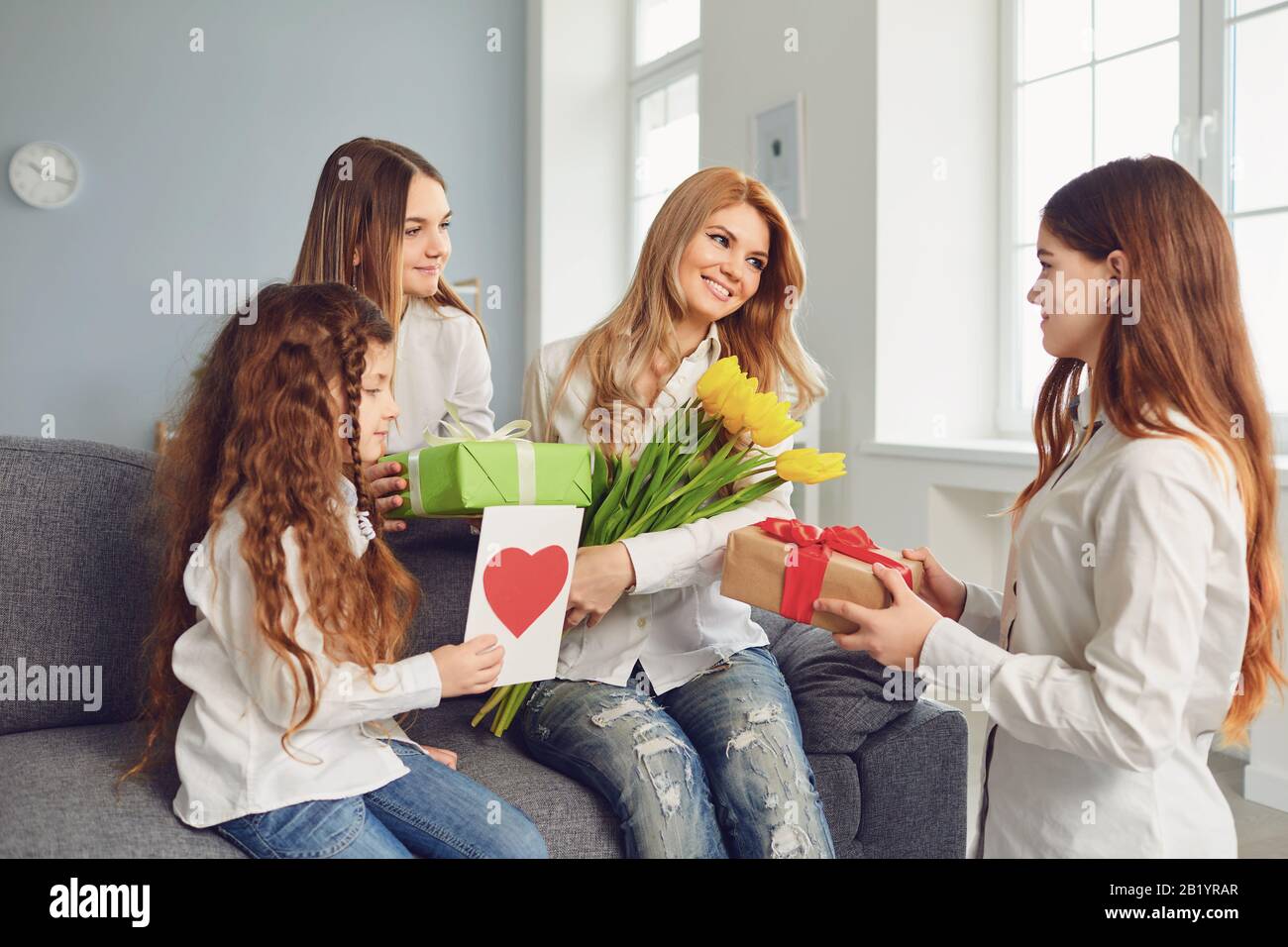 Buona Festa Della Mamma. Le figlie dei bambini danno al mom un mazzo di fiori a casa. Foto Stock