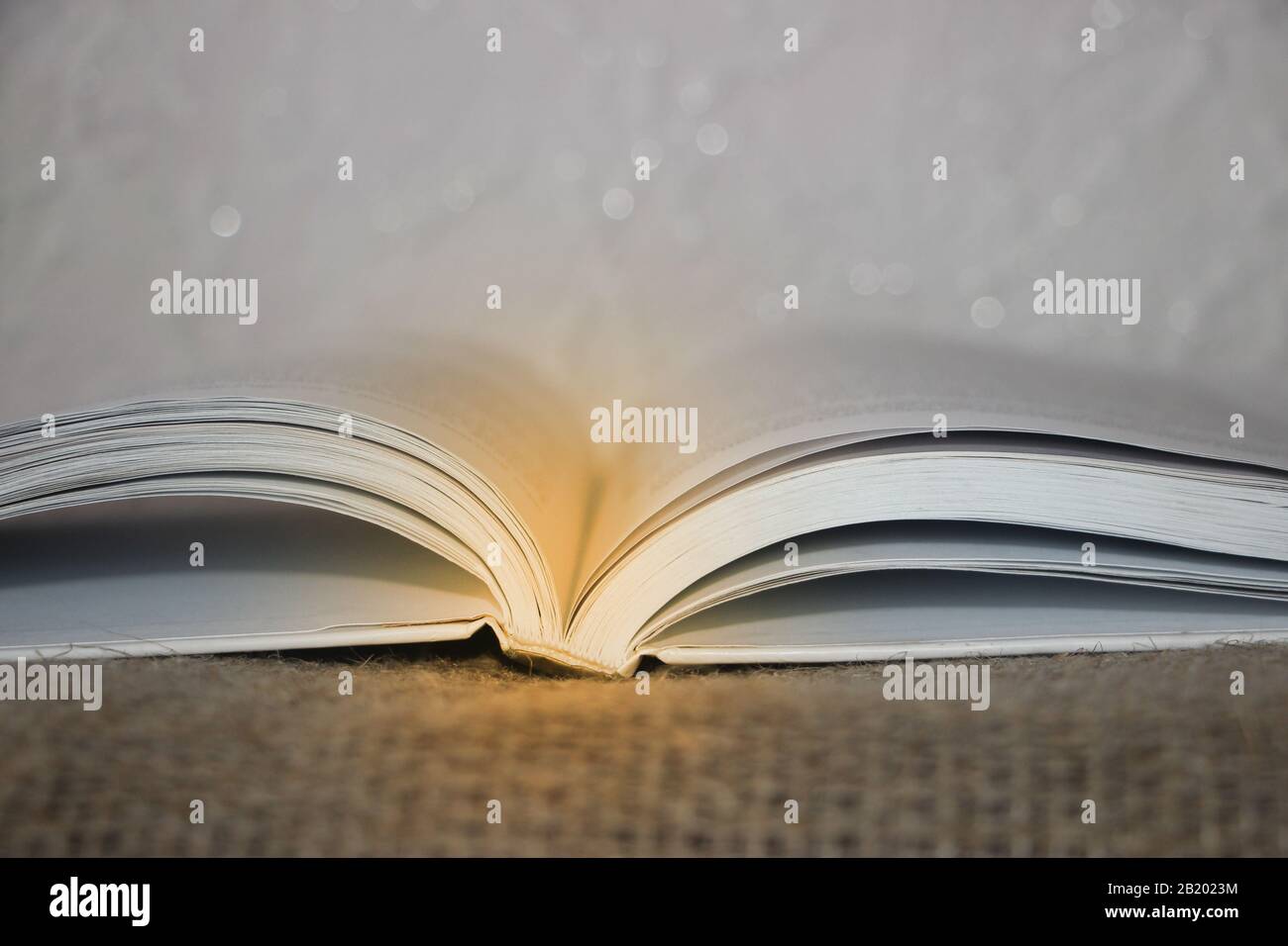 Libro aperto con fascio luminoso su sfondo tela Foto Stock