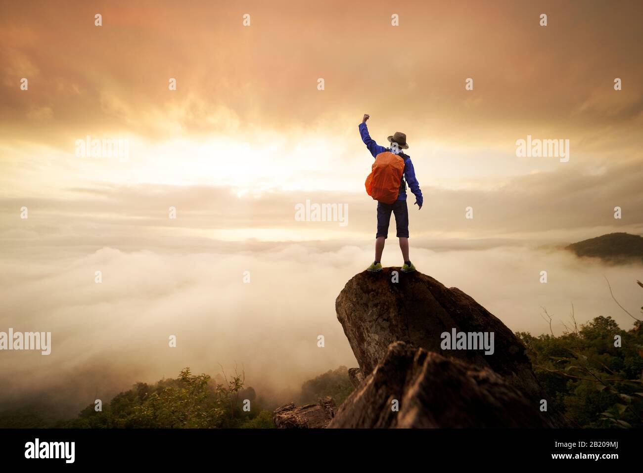 Backpacker uomo sollevare mano su in cima alla montagna con cielo sole e nebbia backgeound Foto Stock