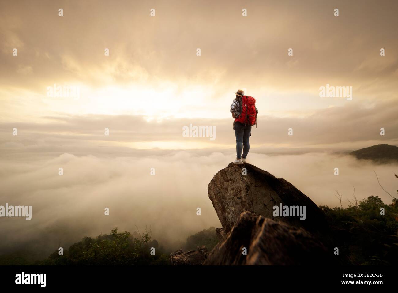 Backpacker donna sollevare mano sulla cima della montagna con il cielo sole e nebbia backgeound Foto Stock