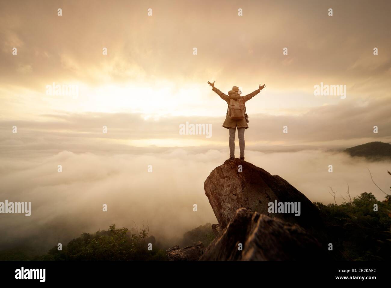Backpacker donna sollevare mano sulla cima della montagna con il cielo sole e nebbia backgeound Foto Stock