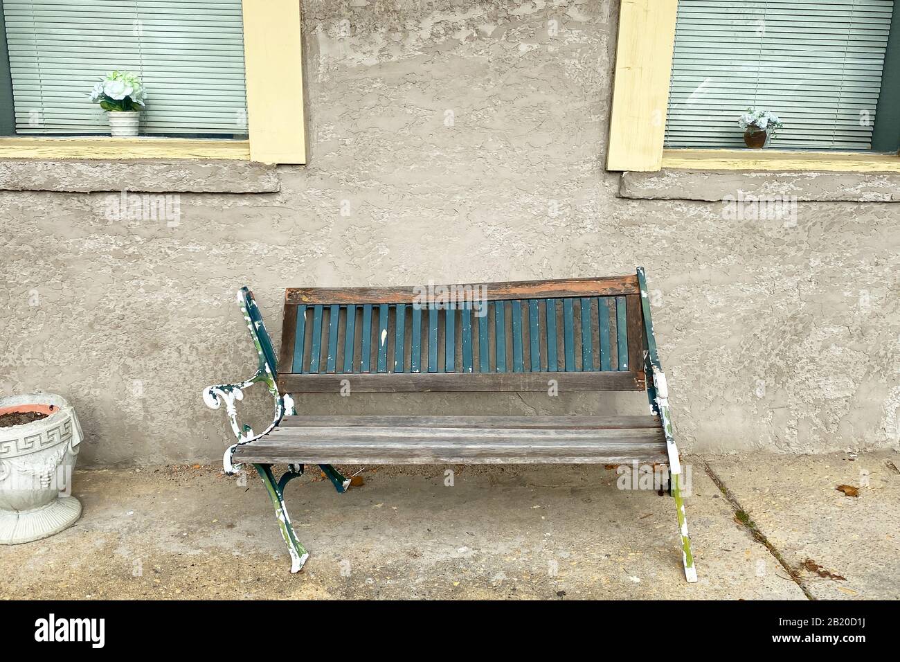 rotto metallo afflitto e legno verde e panca bianca contro un muro di stucco con finestre con cornice gialla Foto Stock