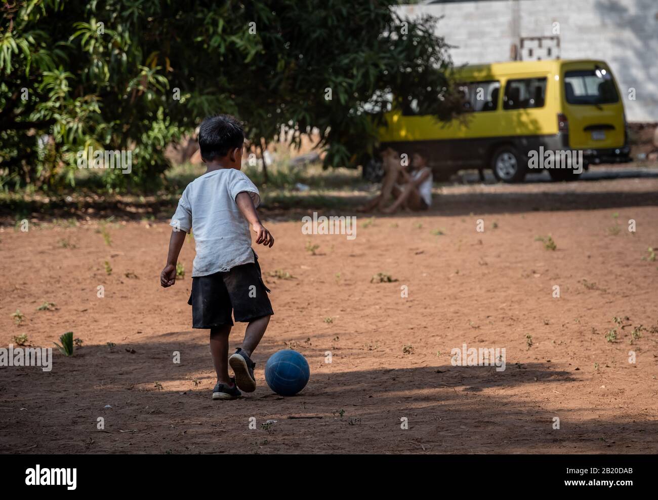 Giovane bambino ispanico che corre con calcio / calcio su campo di sporcizia nel villaggio guatemalteco Foto Stock