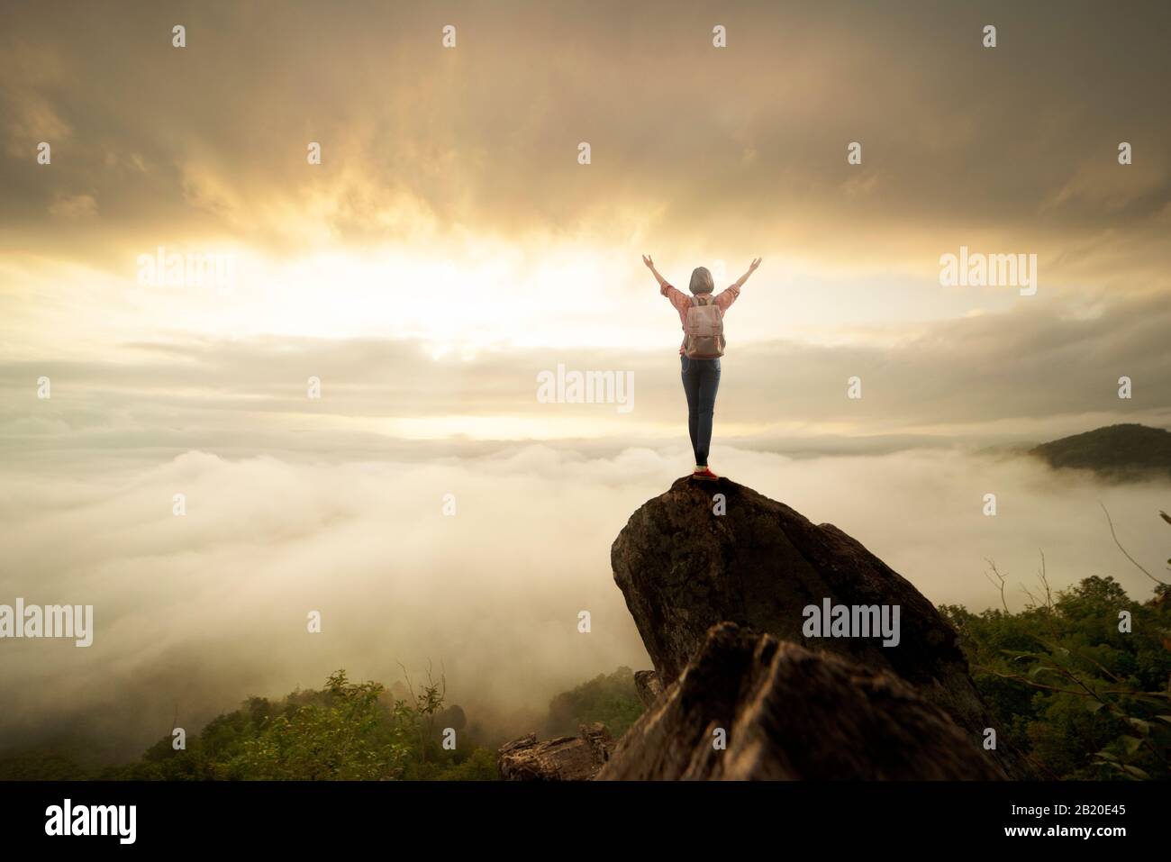 Backpacker donna sollevare mano sulla cima della montagna con cielo sole e nebbia sfondo Foto Stock