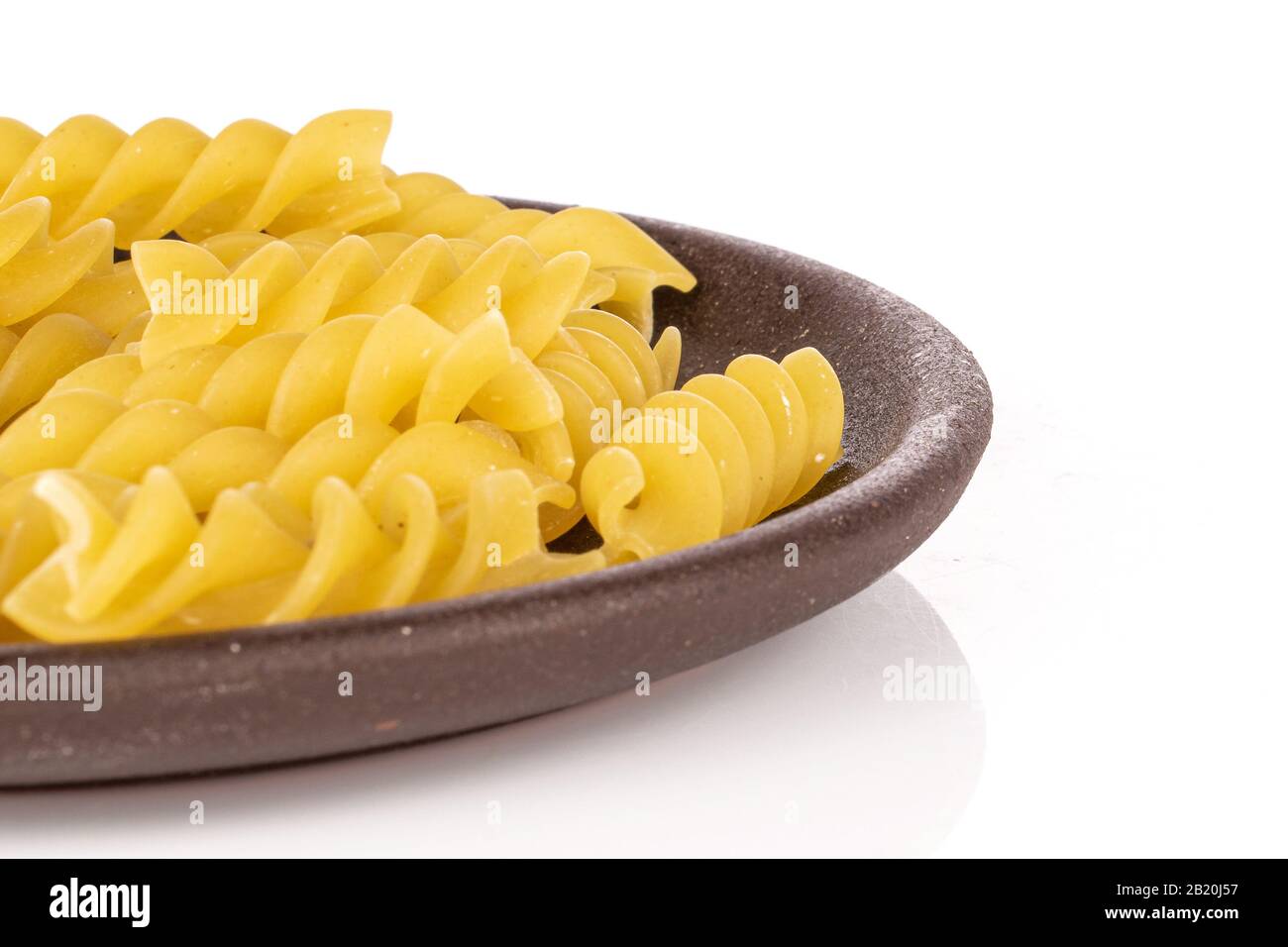 Molta pasta gialla intera fusilli con montagne russe di ceramica marrone isolate su sfondo bianco Foto Stock